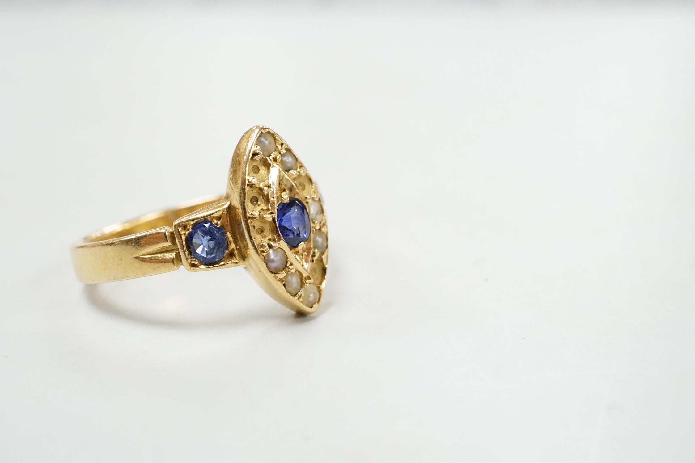 An early 20th century yellow metal, sapphire and seed pearl set marquise cluster ring (pearls missing), size L/M, gross weight 3.6 grams.